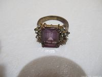 Front-facing view of the vintage amethyst ring showing the large rectangular purple amethyst center stone with clear accent stones on each side, set in a gold-tone band.