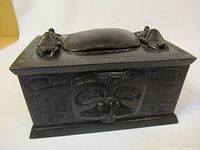 Angled front view showing rectangular box with carved relief face motif on front panel and textured side patterns