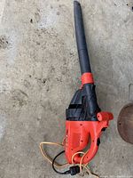 Full view of Black & Decker electric leaf blower on concrete floor showing handle, trigger, blower tube, and power cord