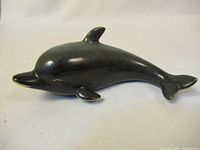 Side view of a glossy black ceramic dolphin figurine showing the smooth body and dorsal fin.