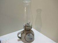 Full view of vintage ceramic oil lamp showing base, handle, metal burner, and glass chimney.