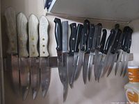13 knives with white textured, black plastic, and large black grip handles on magnetic knife strip.