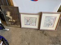 Lot of three framed artworks including two floral still life watercolors and one portrait of a child. The child portrait has an ornate wooden frame and is behind glass. Floral prints have double matting and matching wooden frames.