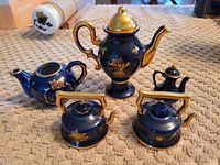 Group photo showing five Limoges porcelain miniatures including coffee urn, slender teapot, and three small kettles, all dark blue with gold floral details and gilded accents.