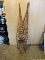 Pair of vintage wooden snowshoes leaning against a wall, showing full length and webbing pattern