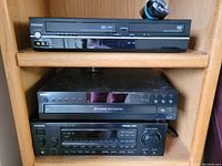 Photo showing three items stacked in a wooden shelf: Toshiba VHS/DVD combo player, Sony DVD player, Kenwood stereo receiver.