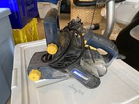 Side view of Mastercraft belt sander showing black body, yellow adjustment knobs, handle, and power cord, placed on white container.