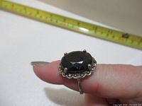Close-up front angle of black onyx ring with six-prong silver setting and decorative scalloped bezel, showing front detail and size relative to tape measure.