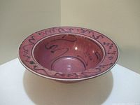 Full view of ceramic bowl showing reddish-pink glaze and black abstract line designs around rim and in center.