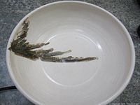Interior view of the bowl showing the white glaze and abstract botanical painting in green and brown.