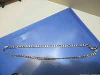Full view of the silver Figaro chain necklace laid flat on a surface.