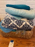 Wicker basket filled with assorted blankets in various blue tones and patterned fabric