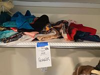 Side view of folded assorted scarves showing various colors and materials stacked on shelf.