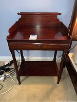 Front view of the dark wooden end table showing top surface, raised gallery back, drawer front, turned legs and lower shelf