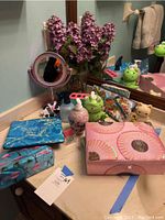 Pink fabric covered jewelry box, makeup bags with ocean and flamingo designs, decorative green frog soap dispensers, countertop mirror, faux pink flowers on bathroom counter.