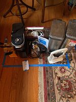 Lot laid out showing the coffee maker, hand mixer, knife block with knives, bread slicer, coffee warmer and two garbage cans on a carpeted floor.