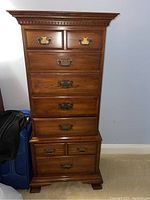 Front view of tall dark wooden lingerie chest with seven drawers and detailed crown molding.
