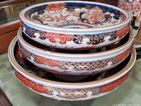 Stacked view of three footed Imari-style bowls showing the exterior designs and color patterns.
