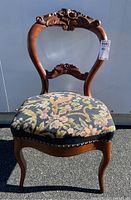 Front view of balloon back chair showing wood carved floral detail and floral upholstered seat.
