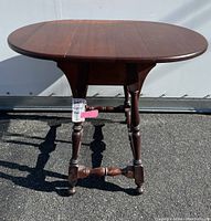 Front view of wooden drop leaf table showing oval shaped top with two leaves and turned legs.