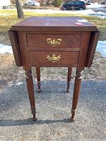 Front view of wooden end table showing two drawers with brass handles and closed drop-leaf sides