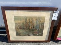 Framed art piece showing a forest river scene with trees and a pink canoe, mounted with beige fabric mat and dark wood frame.