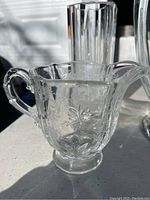 Small glass pourer with handle and floral etching in clear glass, visible chips and scratches