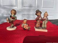 Three Hummel figurines shown side by side on red cloth in front of a door, clearly showing general condition and poses.