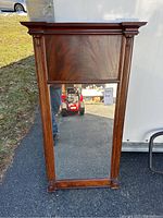 Front view of the wooden framed mirror showing its decorative design and polished wood grain on upper panel.
