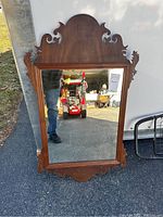 Front view of carved wooden mirror showing full frame and reflective glass with ornate carved top crest and side details.