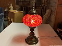 Photo of a red mosaic table lamp lit on a table with visible ornate metallic base and glowing glass mosaic shade.