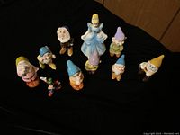 Top view of all nine Disney porcelain figurines on a black cloth background, featuring Cinderella and the seven dwarfs along with Goofy
