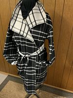 Front view of reversible black and white plaid wool coat with belt tied at waist, displayed on mannequin.