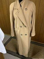 Front view of camel-colored long wool double-breasted coat with six buttons and side flap pockets.