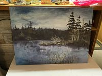 Front view of the oil painting showing a lake, trees, and cloudy sky in muted natural colors. Signature visible in lower-left corner.