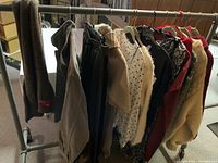 Rack of assorted ladies clothing hung on a rack including sweaters, jackets, pants, and tops in various colors and patterns.
