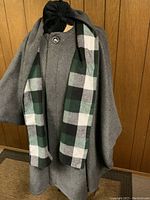 Solid grey side of the reversible wool and flannel cape displayed on a dress form, showing a button near the neck and the flowing shape of the cape.
