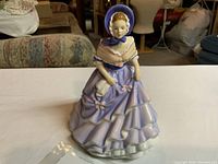 Front view of the Royal Doulton Alice figurine in purple dress and bonnet, showing details of the dress layers and shawl.