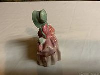 Front and slight side view of Royal Doulton Bo Peep figurine in pink dress and green bonnet, showing the delicate detailing and pastel colors.