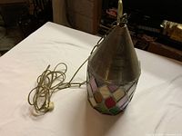 Photo showing stained glass hanging light fixture with heavy metal conical top and attached cord.