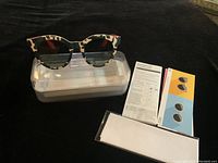 Front view of Swatch glasses placed on clear plastic case with user manuals and cleaning cloth laid out.