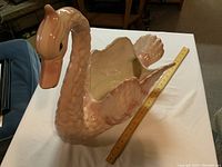 Large pink ceramic swan figurine with a ruler to show length on table surface