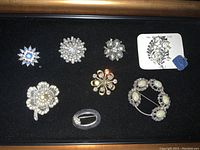 Photo of 8 vintage brooches and pins arranged on a black surface, showing clear detail of their designs.