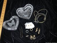 Overview of all lot items including crystal dishes, earrings, rings, on black velvet with measuring ruler.