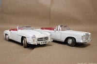 Angled front and side view of two white Mercedes Benz 1/18 scale model cars emphasizing details like wheels, grills, and windshield.