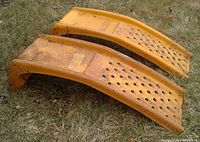 Side angle view of two yellow painted steel auto ramps lying on grass, showing rust and wear on surfaces.