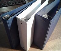View of three binders standing upright showing their ring sizes and covers in navy blue and white.
