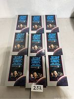 Nine boxed Star Trek The Next Generation VHS movies arranged on floor showing front covers with main Star Trek characters and title.