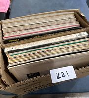 Box containing approximately 30 vinyl records in paper sleeves and album covers, with various titles.