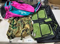 Three bags on a table: large green/black duffle, pink/teal Spalding duffle, and camouflage drawstring bag.